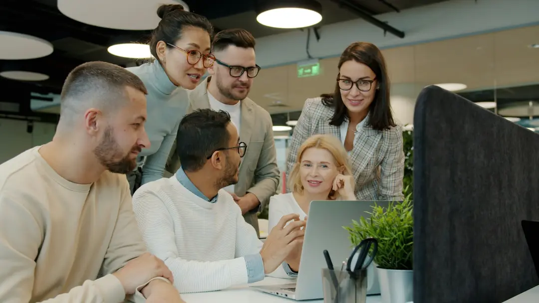 A team gathered around a laptop in an open-plan office, discussing what’s on the screen