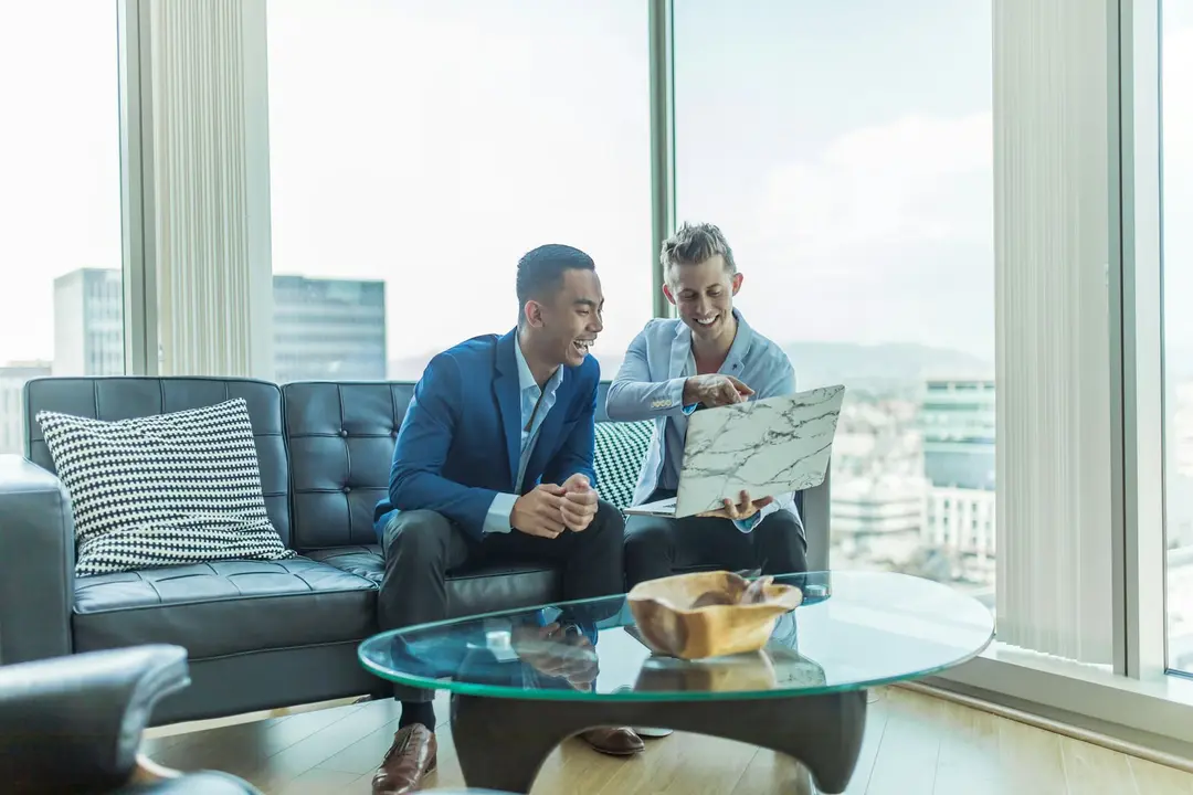 Two real estate agents reviewing a listing on a laptop in a bright office
