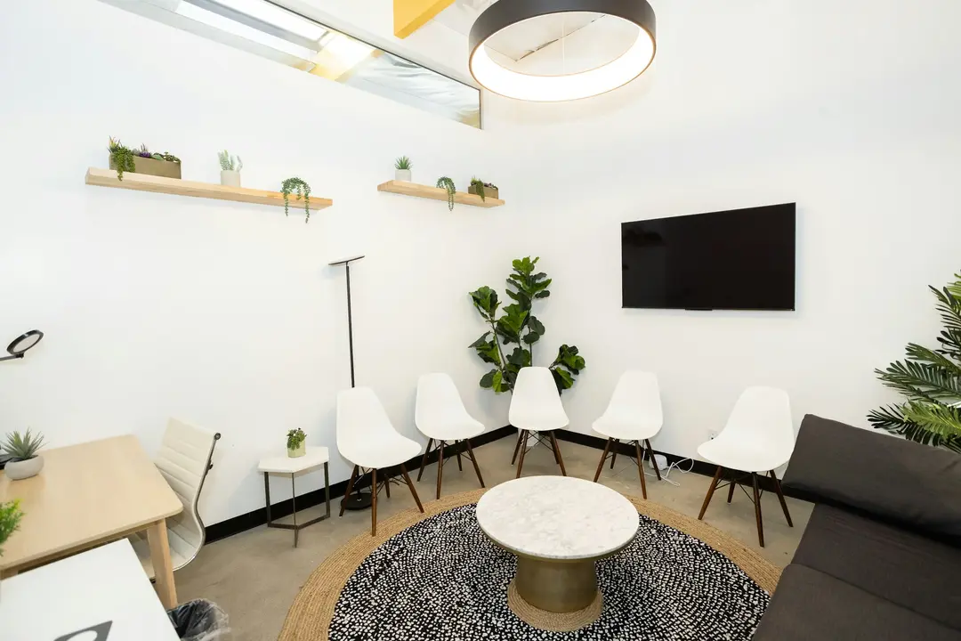 A clinic waiting room with white chairs and plants