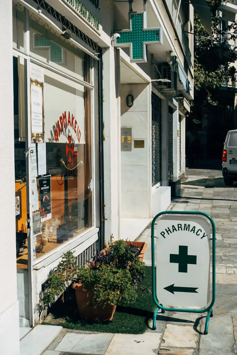 A pharmacy shopfront on a sunny street with a green cross sign