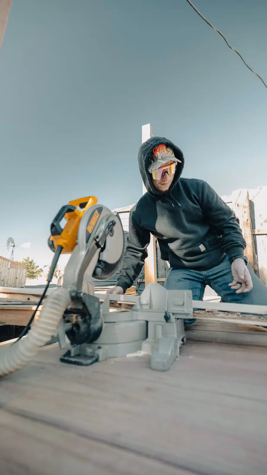 A tradie in safety glasses cutting timber on a mitre saw on site
